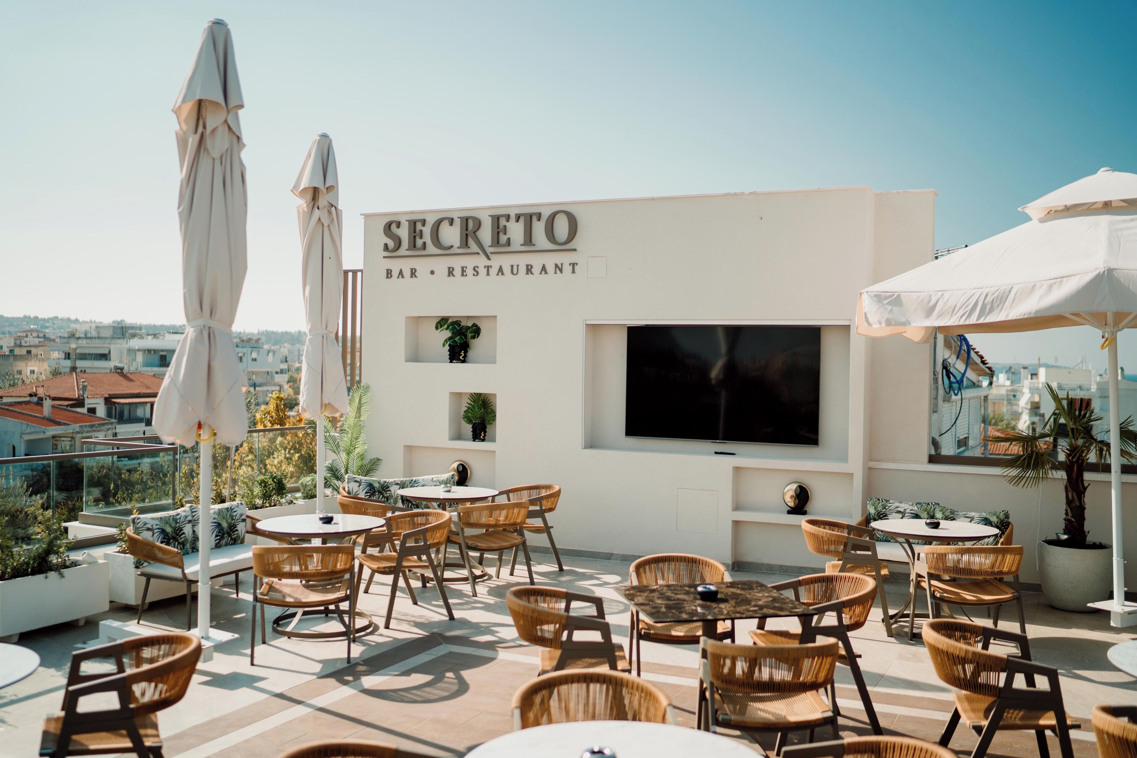 An outdoor seating area with wicker chairs and white umbrellas at a bar and restaurant named SECRETO.