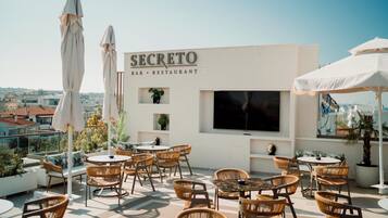 An outdoor seating area with wicker chairs and white umbrellas at a bar and restaurant named SECRETO.