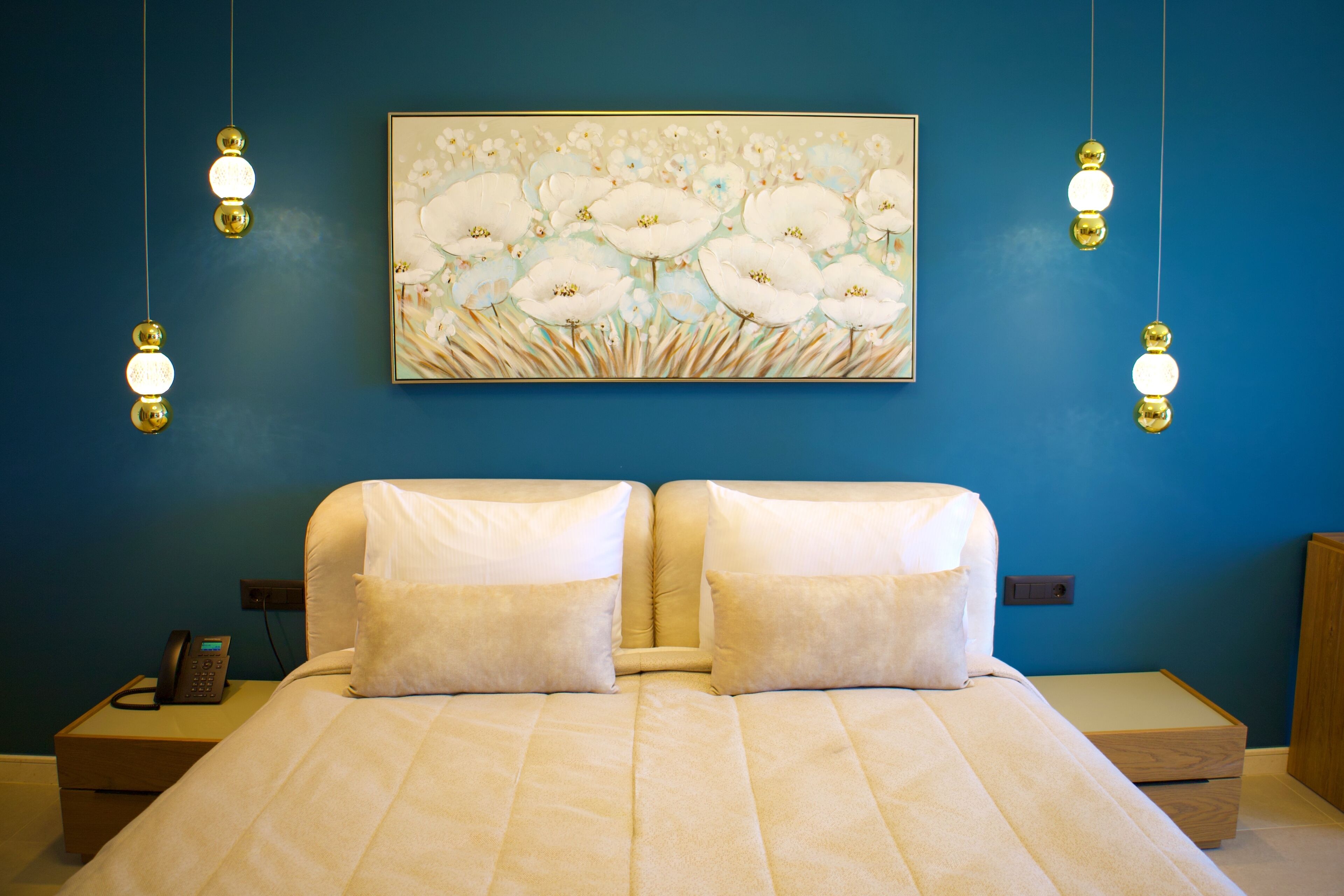 A bedroom with a bed, two bedside tables, a painting, and hanging lights.