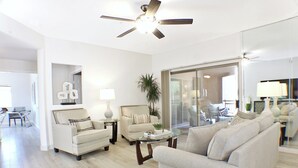 A modern living room with a ceiling fan, a glass coffee table, and two sofas. - 3BR condo near WestWorld (Scottsdale)