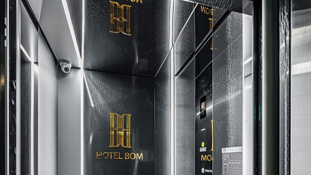 A modern elevator interior with metallic walls, a glass door, and the text "HOTEL BOW" and "HOTEL BOW" on the wall. - Hotel Bom (Pohang)