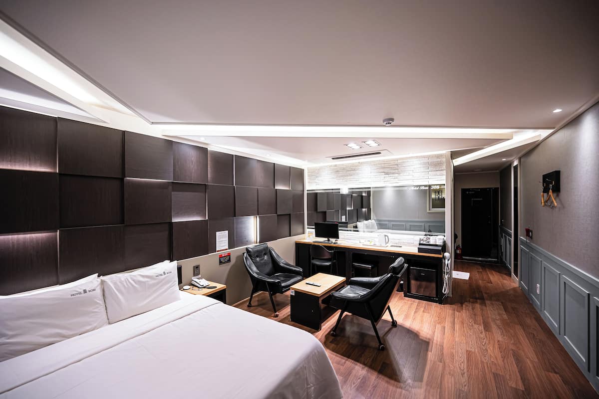 A modern hotel room with a large bed, a desk, and a seating area.