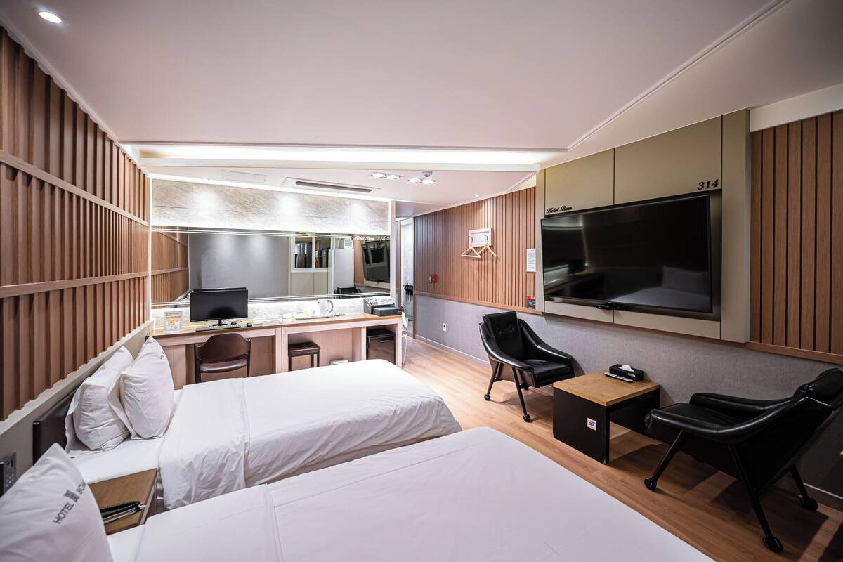 A hotel room with two beds, a desk with a computer, a TV, and a seating area with chairs.