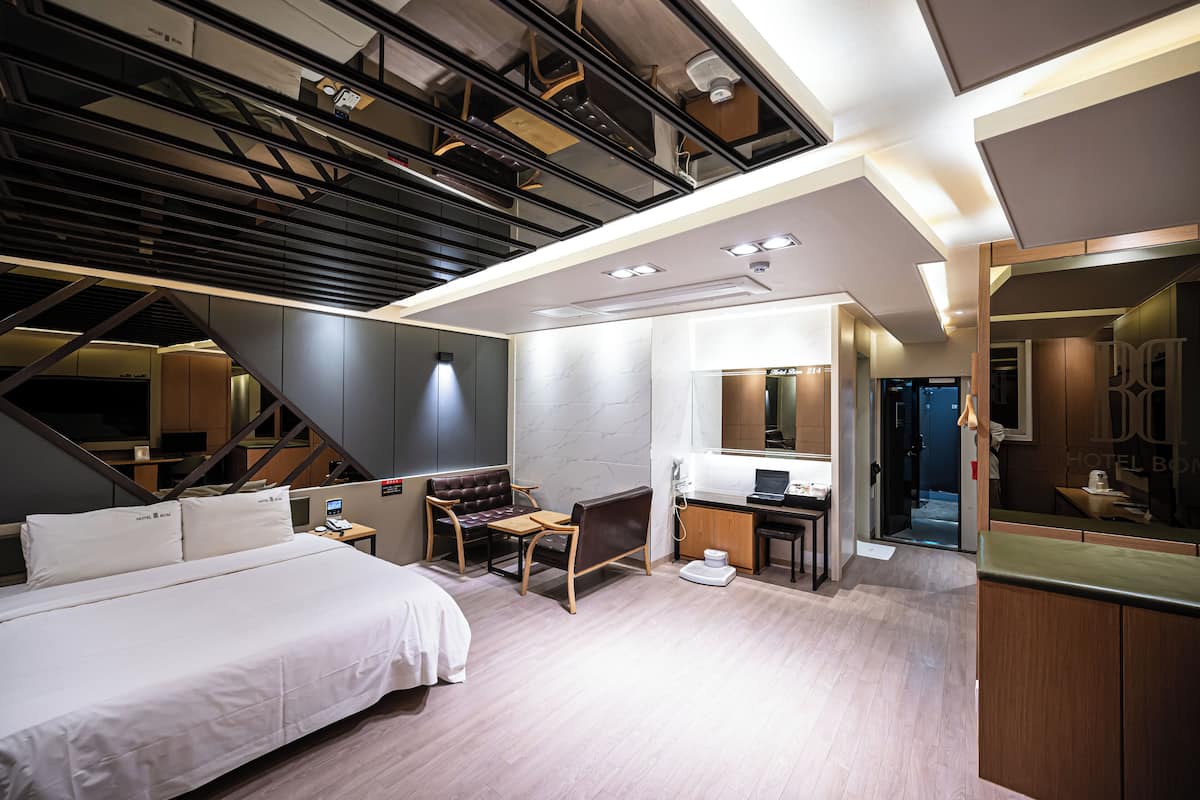 A modern hotel room with a bed, desk, chair, and a large mirror.