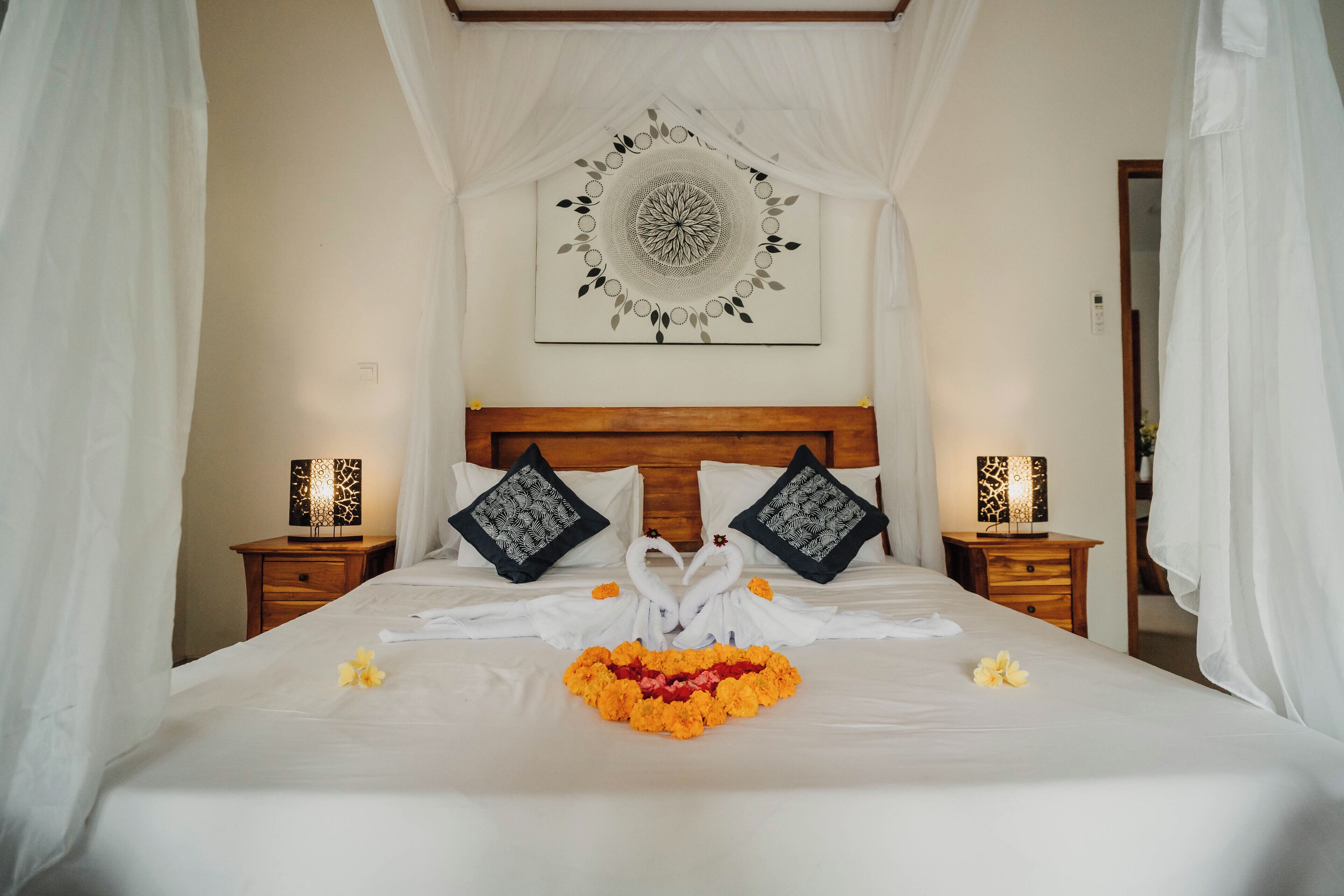 A neatly made bed with a decorative swan pillow arrangement, a wall art piece, and a bedside table with a lamp.