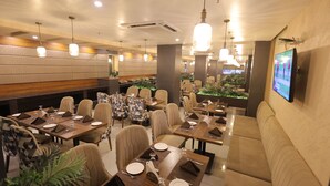 Un restaurant doté de nombreuses tables, de chaises et d’un grand écran diffusant un événement sportif.