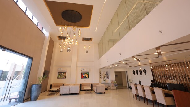 Un hall d’entrée spacieux avec un plafond haut, des luminaires modernes, des coins salon et des œuvres d’art accrochées aux murs.