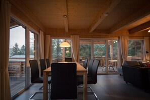 A dining area with a table and chairs, large windows, and a view of the outdoors.