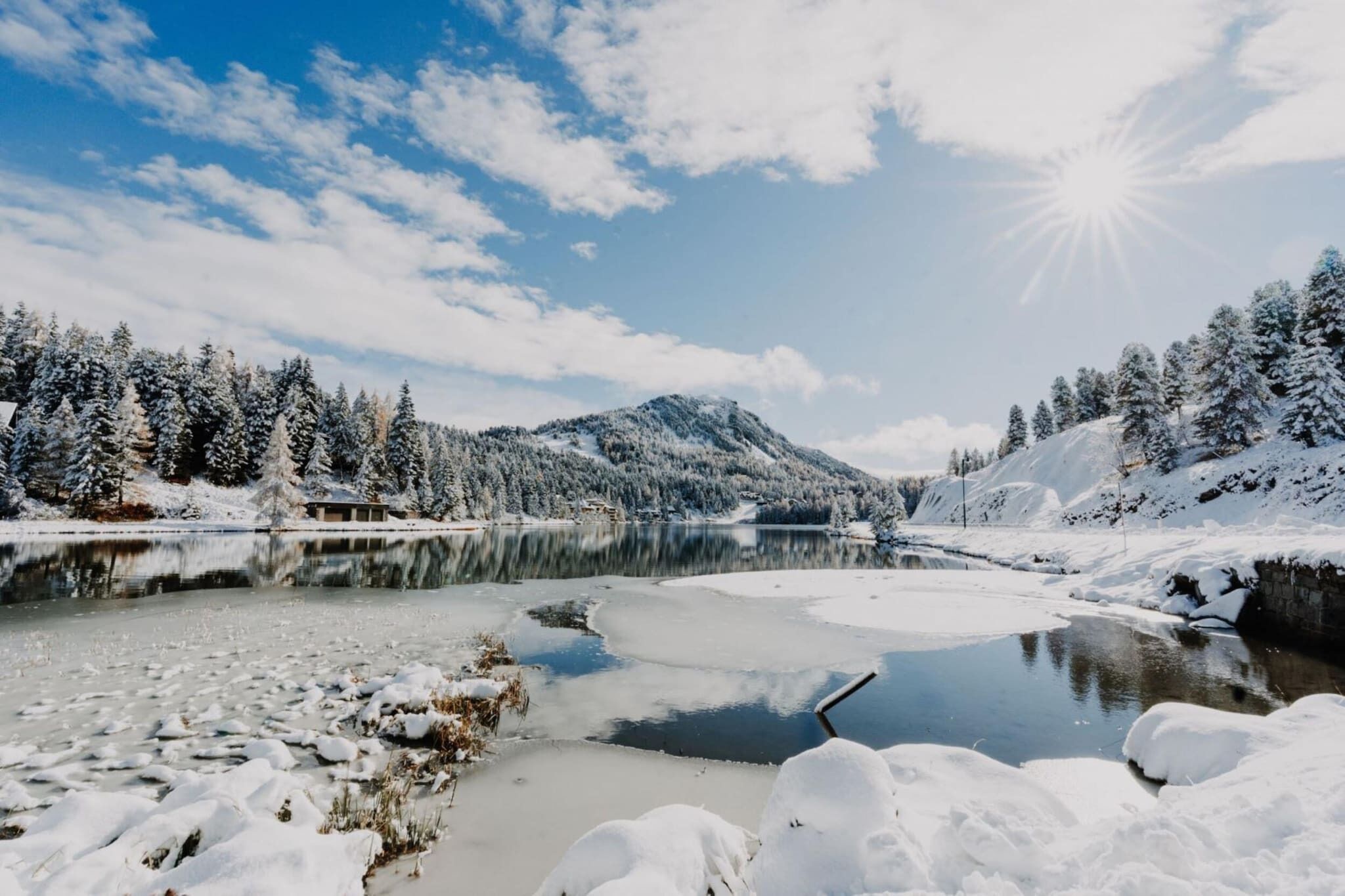 A winter landscape with a frozen lake, snow-covered trees, and mountains in the background.