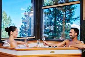 A couple in a modern hot tub with a large window view of trees.