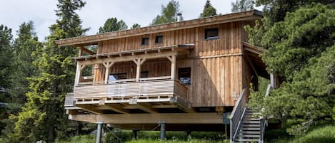Una cabaña de madera con balcón, ubicada sobre pilotes en un área boscosa.