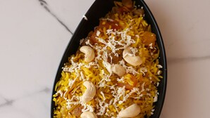 A black oval-shaped dish filled with yellow rice, garnished with cashews and almonds, on a marble surface. - Four Seasons Resort (Adityapur)