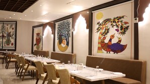 A dining area with long tables, cushioned booths, and wall art depicting birds and trees. - Four Seasons Resort (Adityapur)