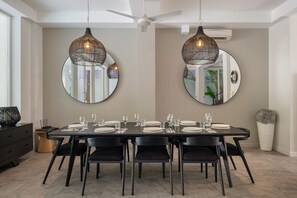 A dining area with a long table set for six, surrounded by black chairs, with two large round mirrors on the walls and a ceiling fan above. - Villa Levi by GORO (Seminyak)