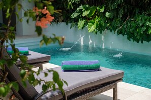 A poolside area with lounge chairs and a water feature. - Villa Levi by GORO (Seminyak)