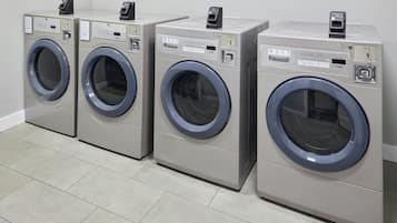 A row of four identical front-loading washing machines in a commercial setting.