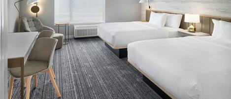 Habitación de hotel con dos camas, un escritorio, una silla y una lámpara.