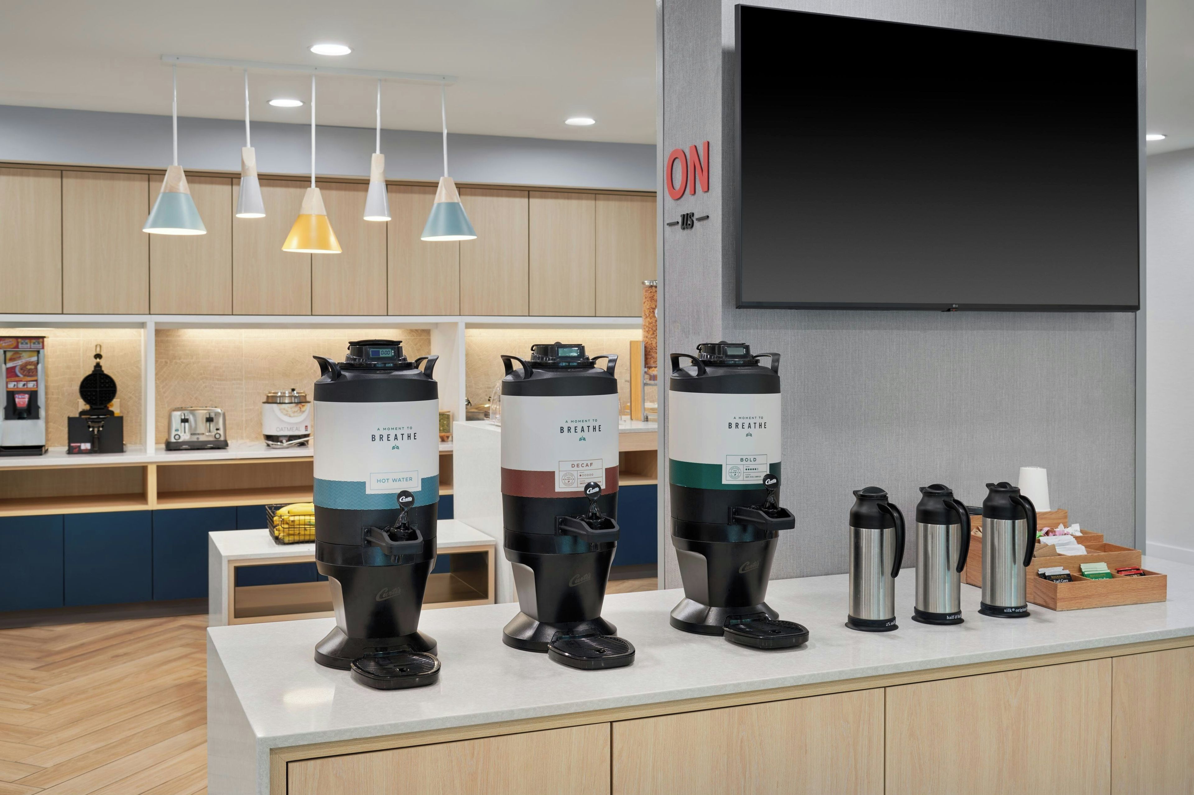 A coffee station with multiple coffee makers and a television mounted on the wall.
