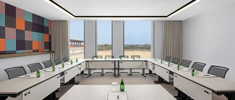 A conference room with a long table, multiple chairs, and a view of the beach through large windows.