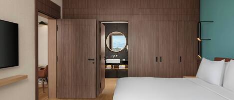Una habitación de hotel moderna con una cama grande, un televisor montado en la pared, un armario de madera y un baño visible a través de una puerta abierta.
