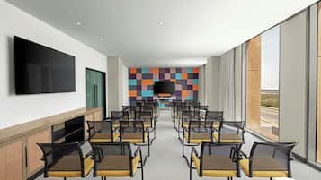 Uma sala de conferências com fileiras de cadeiras, uma grande TV de tela plana na parede e um design de parede colorido.