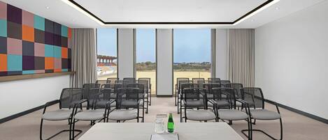 A conference room with a large table, chairs, and a view of a stadium.