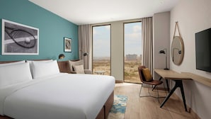 A hotel room with a large bed, a desk, a chair, a TV, and a view of the city. - Four Points By Sheraton Dakar Diamniadio (Diamniadio)