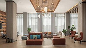 A modern living room with a brown sofa, ottoman, and armchairs, a wooden ceiling, and large windows with sheer curtains. - Four Points By Sheraton Dakar Diamniadio (Diamniadio)