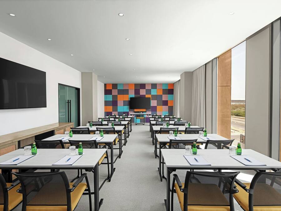 A conference room with tables, chairs, and a large screen.