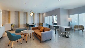 A modern lounge area with a sofa, chairs, and tables, featuring a neutral color palette and ample natural light. - TownePlace Suites by Marriott® Houston Tomball (Tomball)