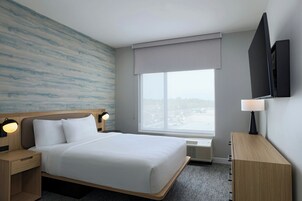 Habitación de hotel moderna con una cama grande, televisor de pantalla plana, mesita de noche con lámpara y ventana con vista a la ciudad.