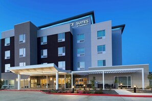 A modern hotel with a sign reading "The Suites by Marriott." It features a multi-story building with a covered entrance and outdoor seating area. - TownePlace Suites by Marriott® Houston Tomball (Tomball)