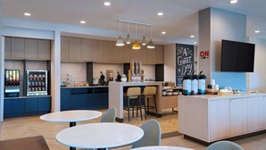 A modern kitchen area with a coffee station, seating area, and a flat-screen TV mounted on the wall. - TownePlace Suites by Marriott® Houston Tomball (Tomball)