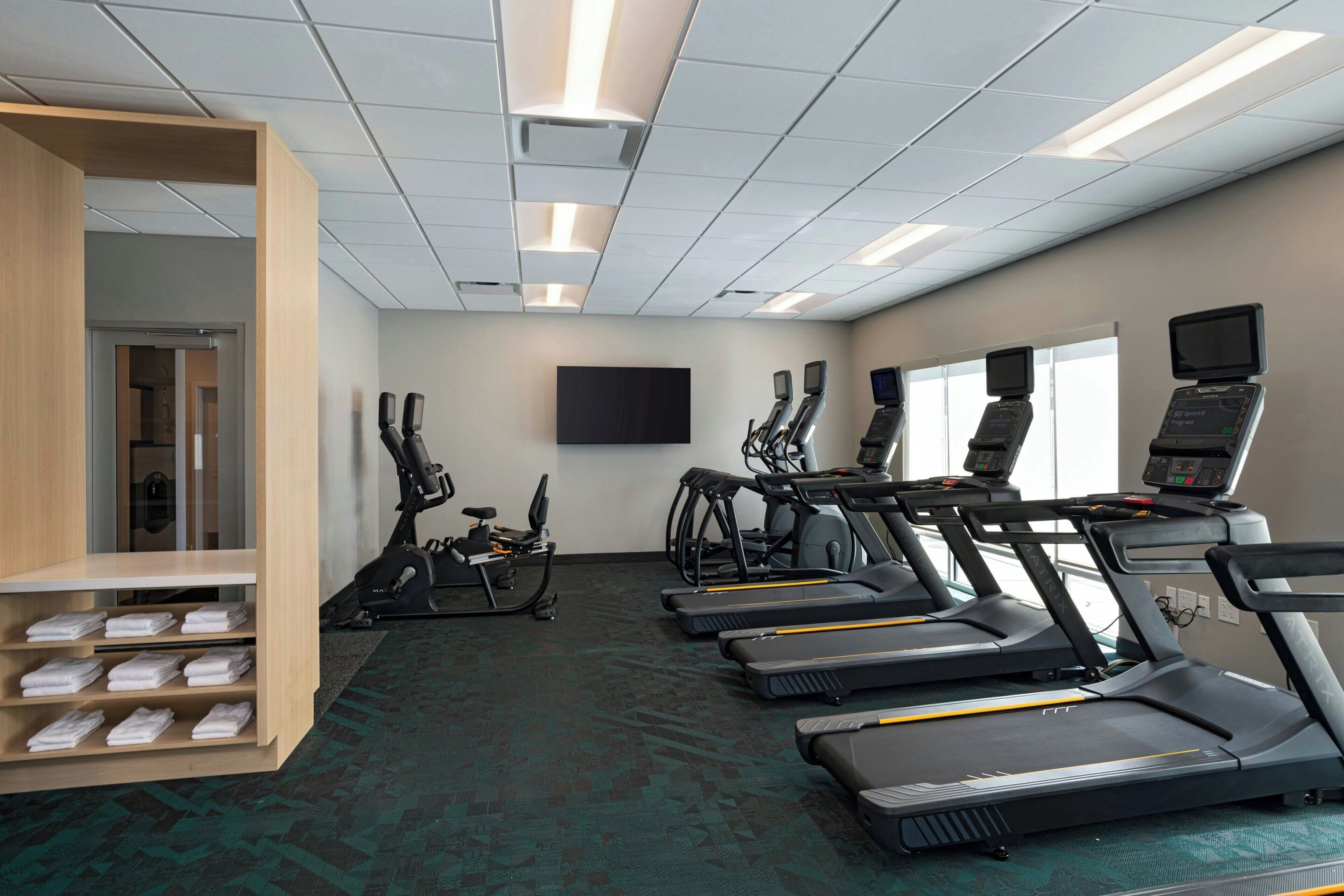 A gym with treadmills, stationary bikes, and a wall-mounted TV.