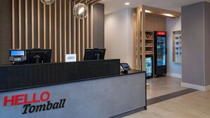 A hotel reception desk with a 'HELLO Tomball' sign, a Lenovo computer, a 'Just Chill' refrigerator, and a vending machine. - TownePlace Suites by Marriott® Houston Tomball (Tomball)