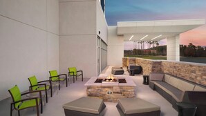 An outdoor patio with a stone fire feature, seating, and chairs. - Springhill Suites By Marriott Raleigh Garner (Garner)