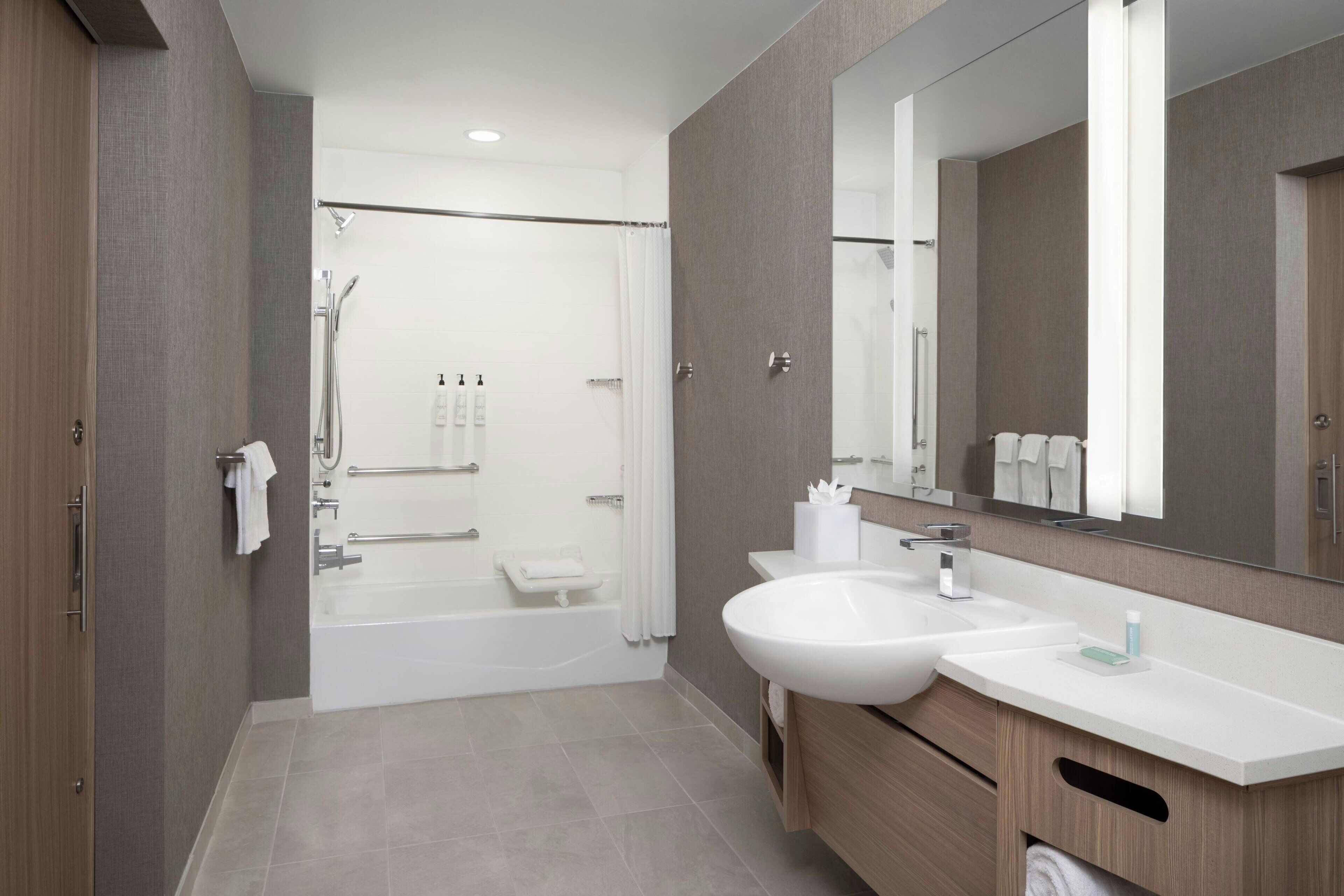 A modern bathroom with a bathtub, a large mirror, and a vanity with a sink.