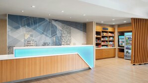 A modern reception area with a wooden counter, a large wall with text, and a vending machine. - Springhill Suites By Marriott Raleigh Garner (Garner)