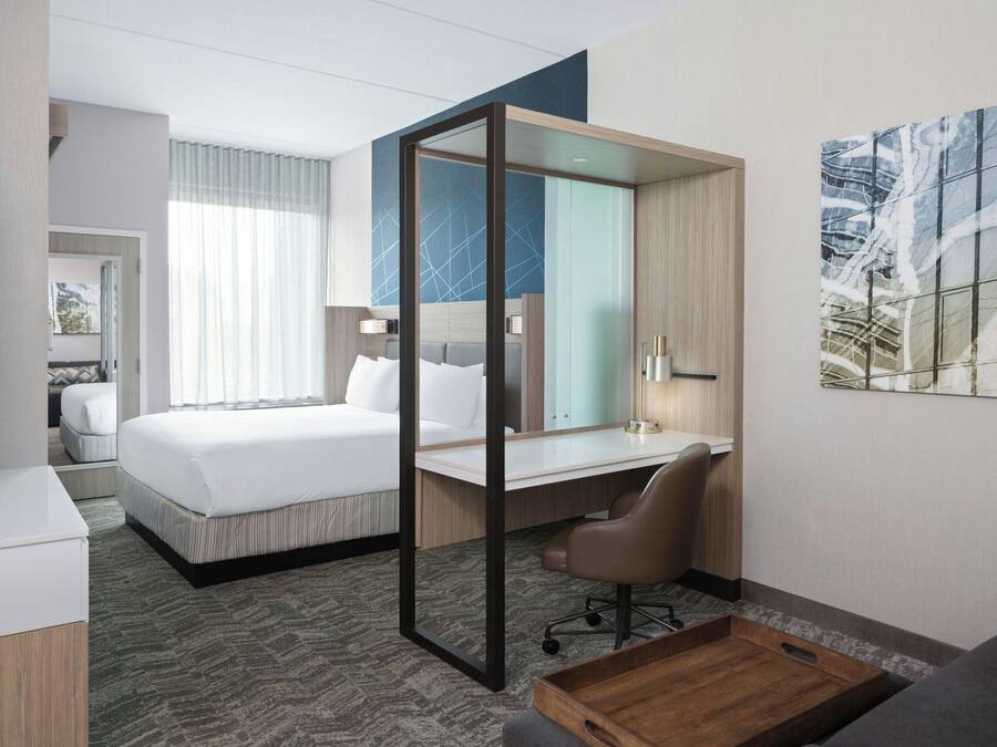 Una habitación de hotel moderna con una cama grande, un escritorio, una silla, un televisor y un cuadro en la pared.