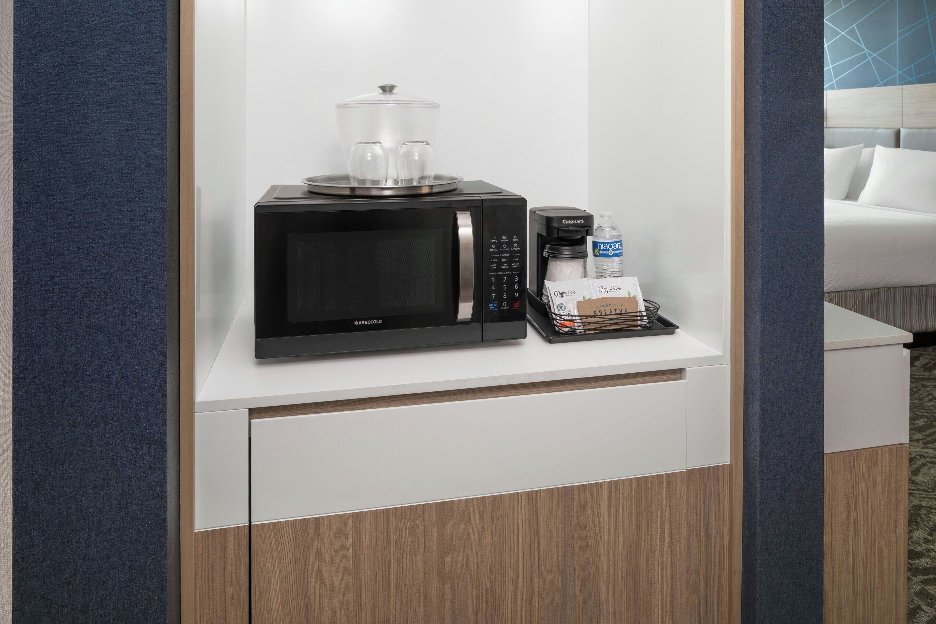A minibar setup with a microwave, a coffee maker, and a bottle of water.