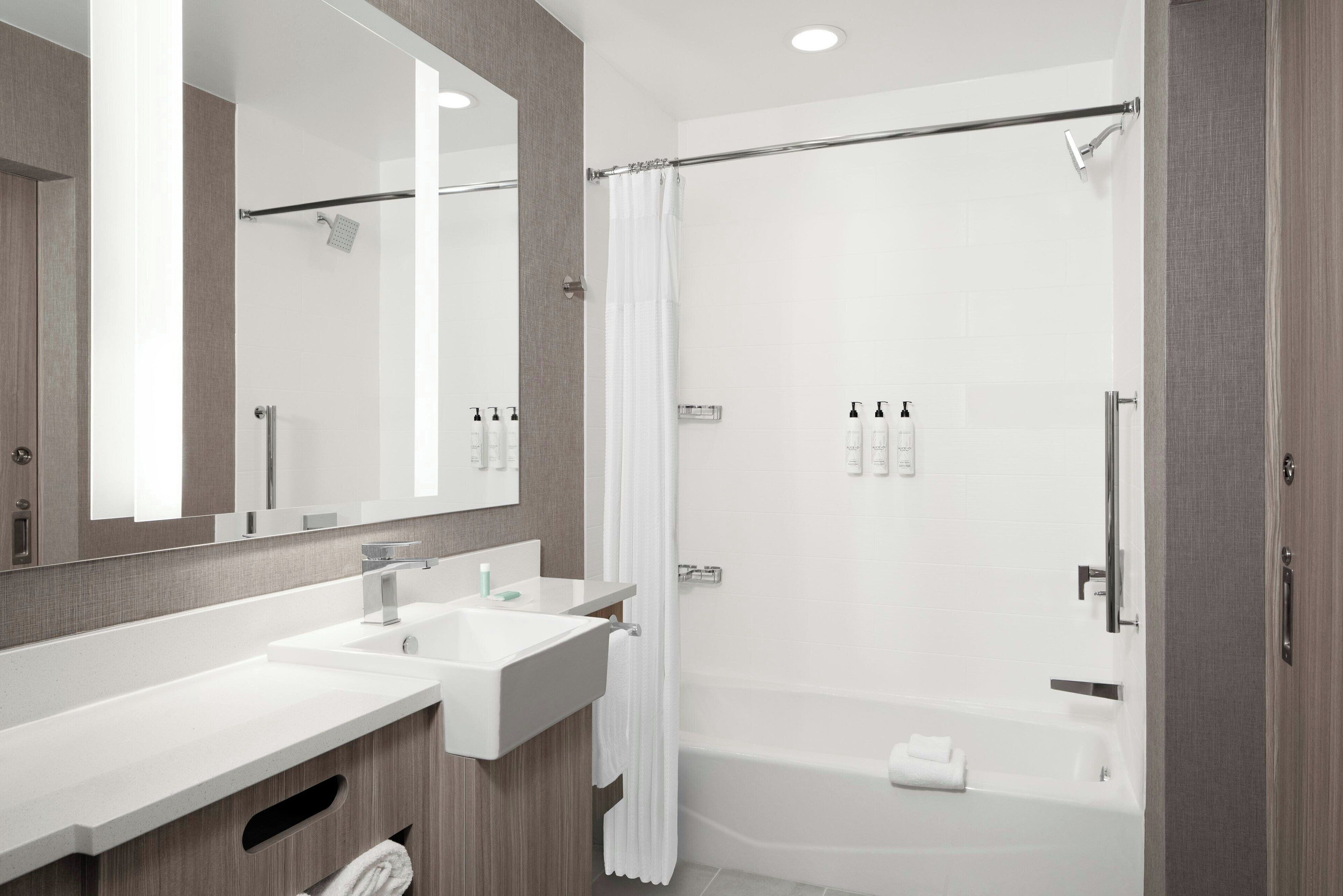 Een moderne badkamer met een grote spiegel, twee wastafels, een douche en een bad.