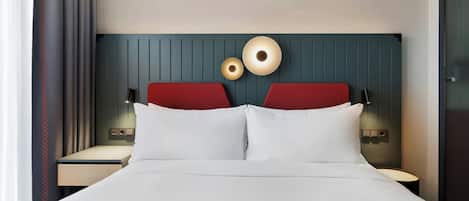 Habitación de hotel con una cama, dos cabeceros rojos, lámparas de noche y una lámpara fijada a la pared.