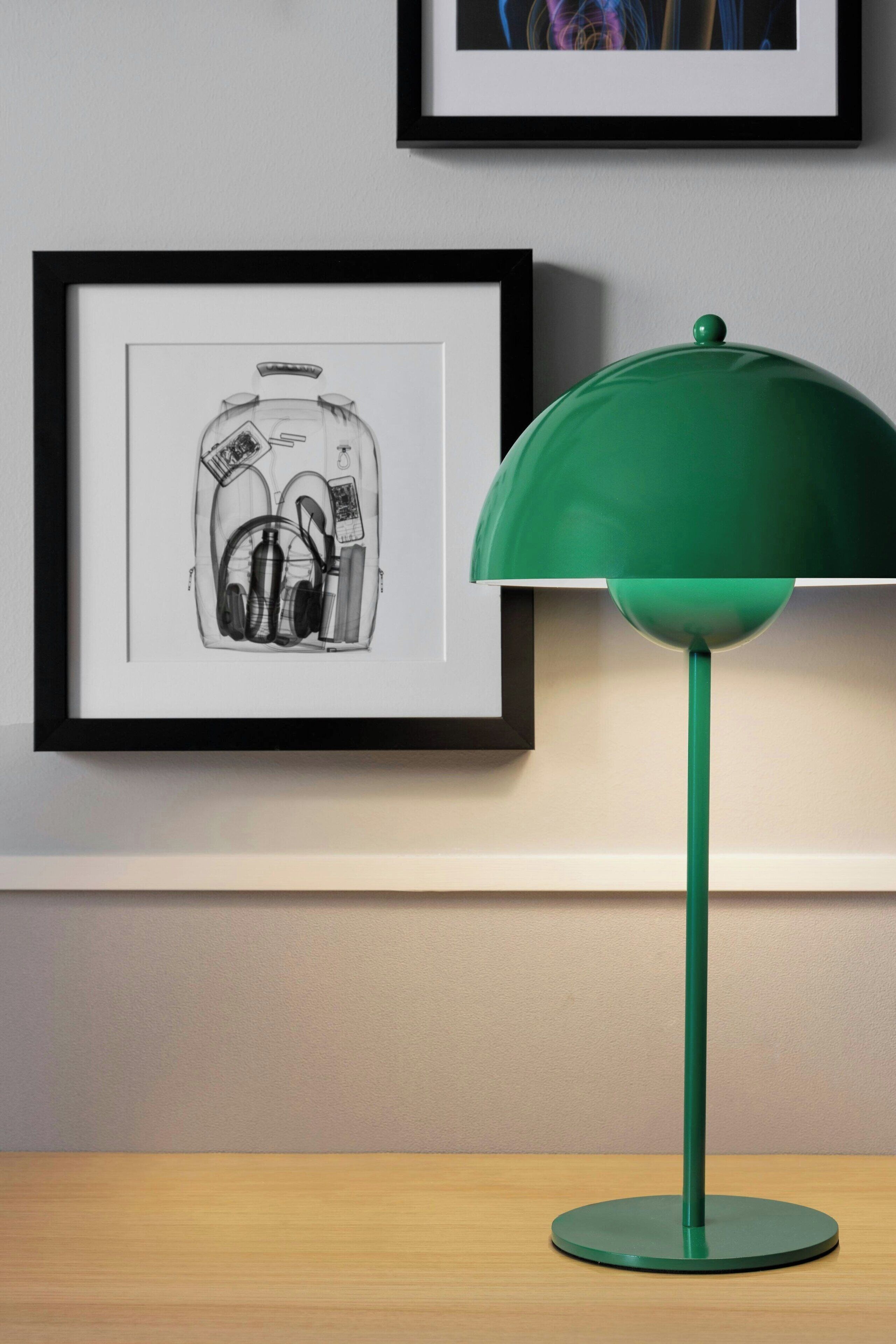 Un dibujo enmarcado de auriculares colgando en una pared, una lámpara verde sobre una mesa y una fotografía enmarcada encima de la lámpara.