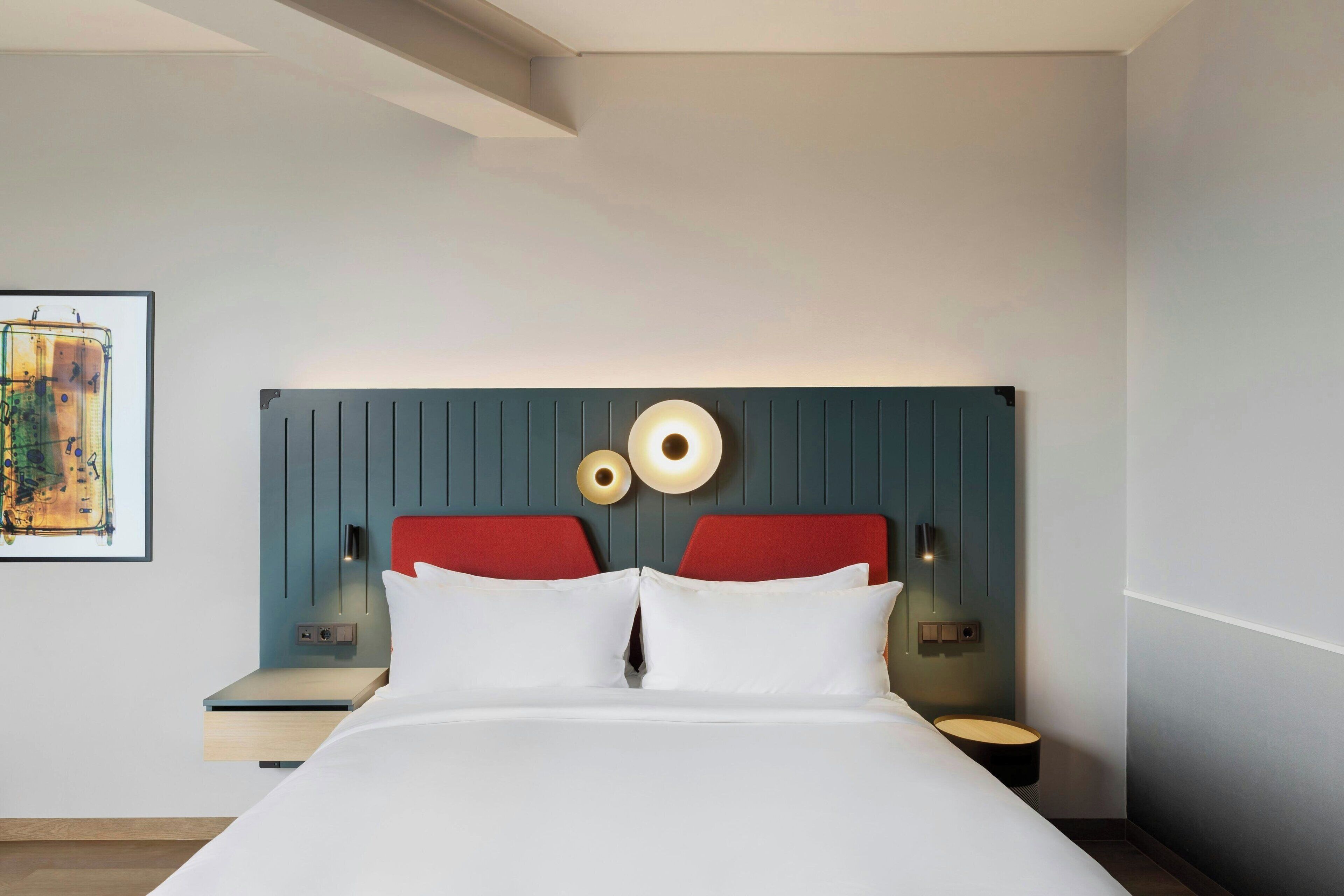 Une chambre d’hôtel moderne, équipée d’un lit, de deux tables de chevet, d’un luminaire fixé au mur et d’un tableau accroché au mur.