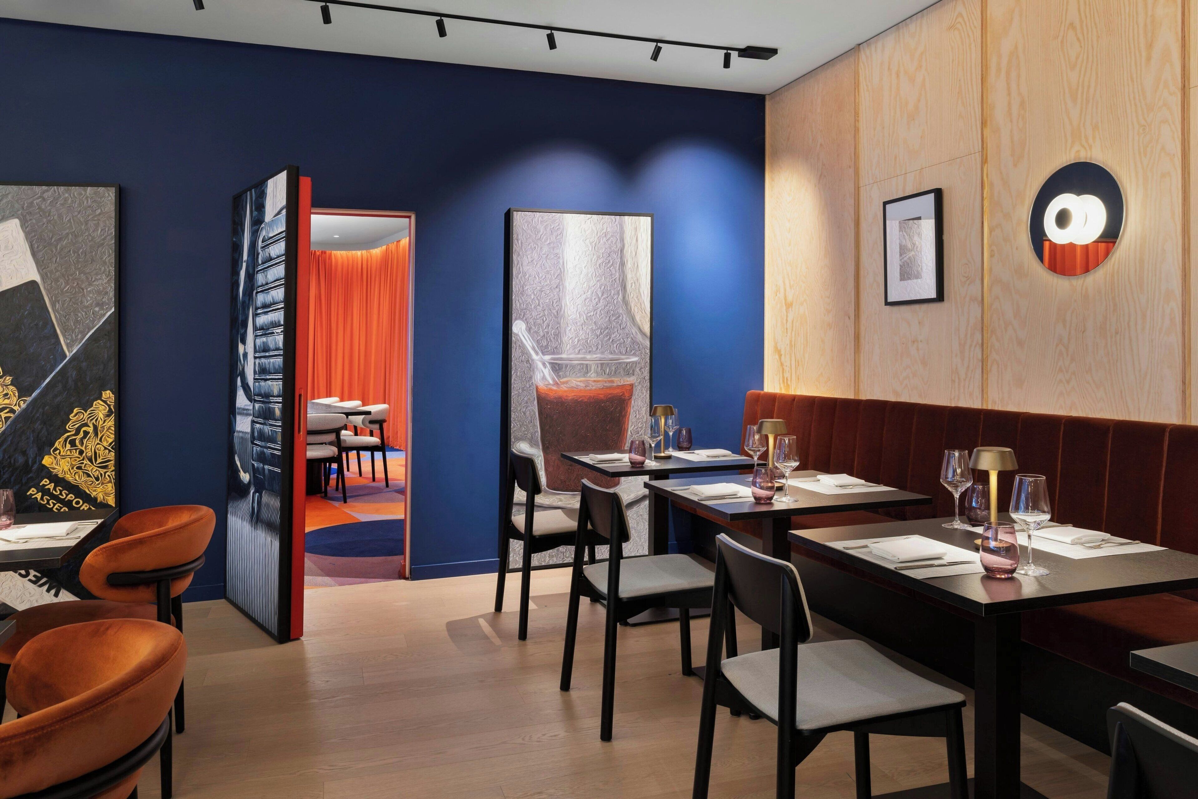 L’intérieur d’un restaurant moderne présente des murs lambrissés en bois, des murs d’accent bleu et des chaises orange. Les tables sont dressées avec des verres à vin et des serviettes.
