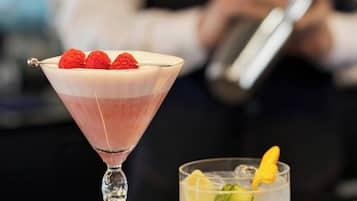 Una copa de martini con una bebida en capas y frambuesas sobre una barra.