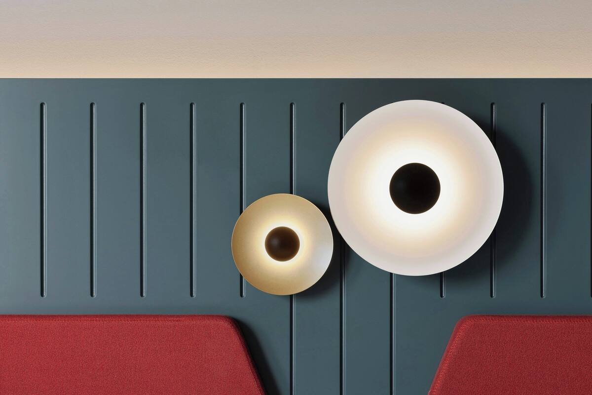 A wall with two wall-mounted light fixtures and a red cushioned bench.