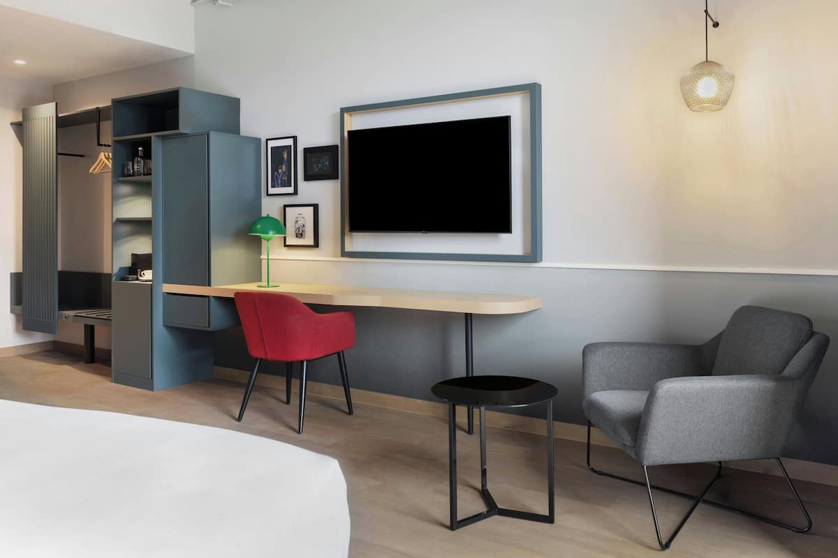 A modern hotel room with a bed, a desk, a chair, and a TV.