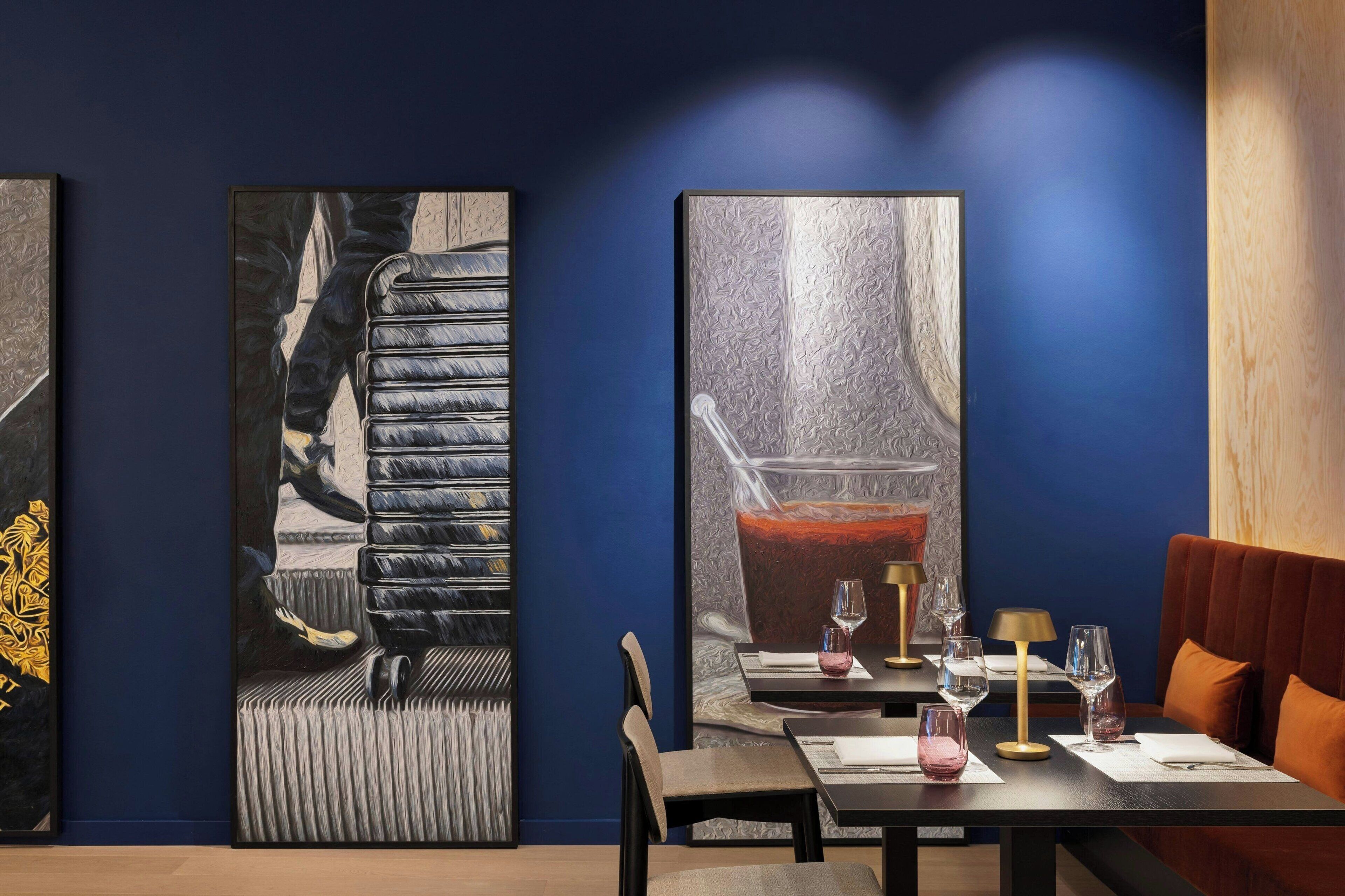 A dining area with a table set for two, two large paintings on the wall, and a wooden panel on the right.