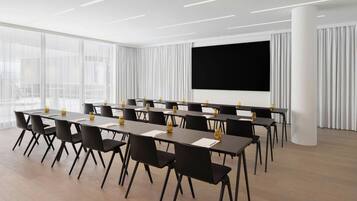 A conference room with a large screen, multiple tables, and chairs.